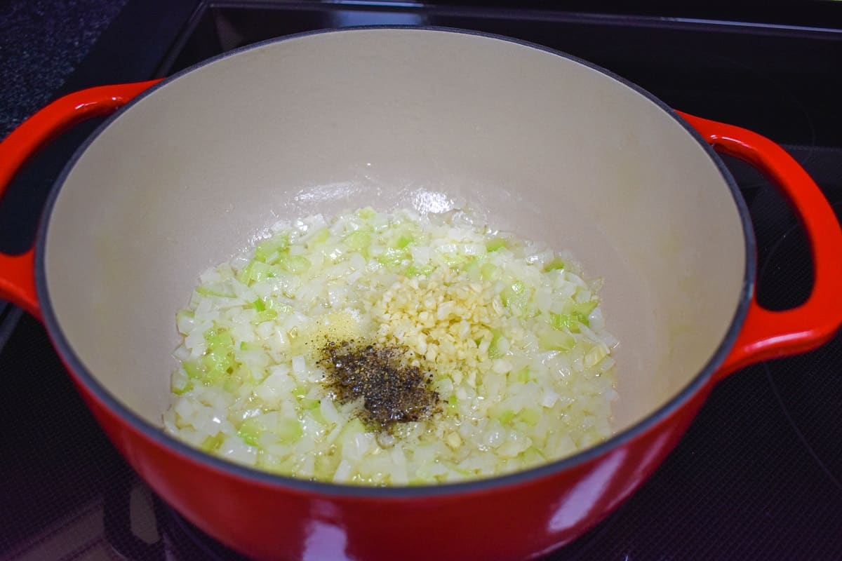 Minced garlic and black pepper added to diced onions and celery sautéing in a large, red pot.