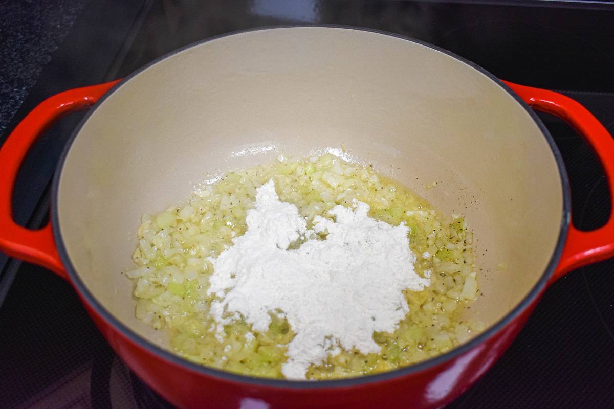 Flour added to the onions, celery, garlic, and spices cooking in a large, red pot.