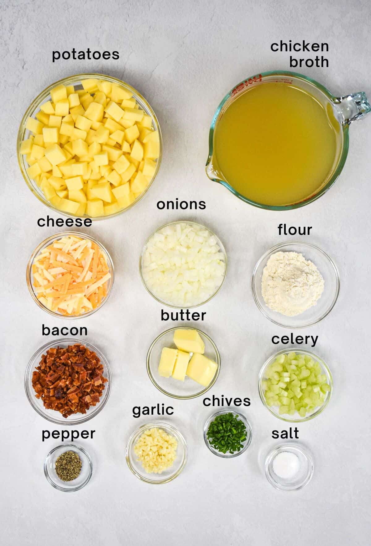 The ingredients for the soup prepped and arranged in glass bowls on a white table with each one labeled with small black letters.