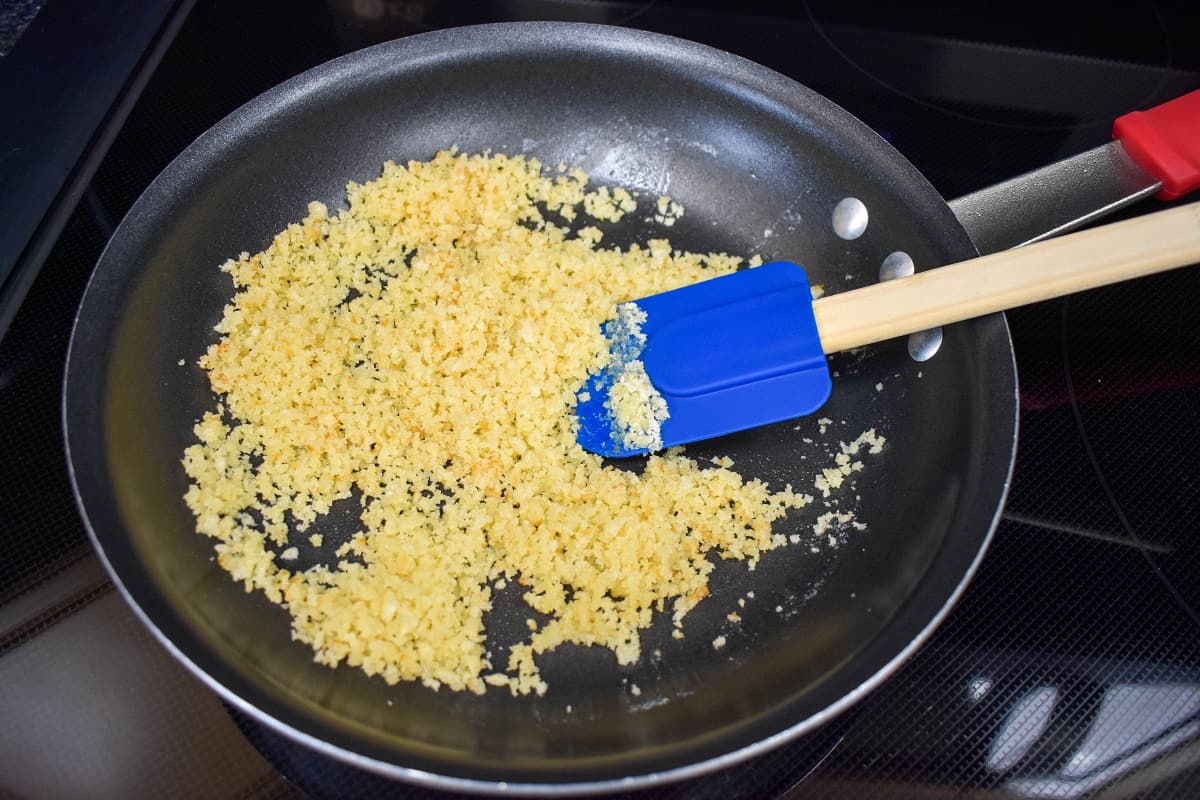 Panko breadcrumbs and butter combined in a non-stick skillet with a blue silicone spatula.