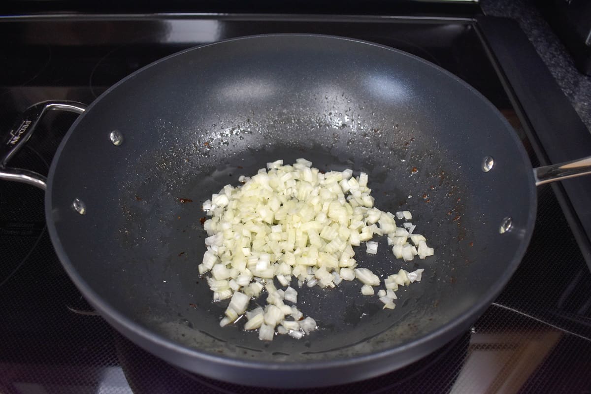 Diced onions cooking in a large, non-stick skillet.