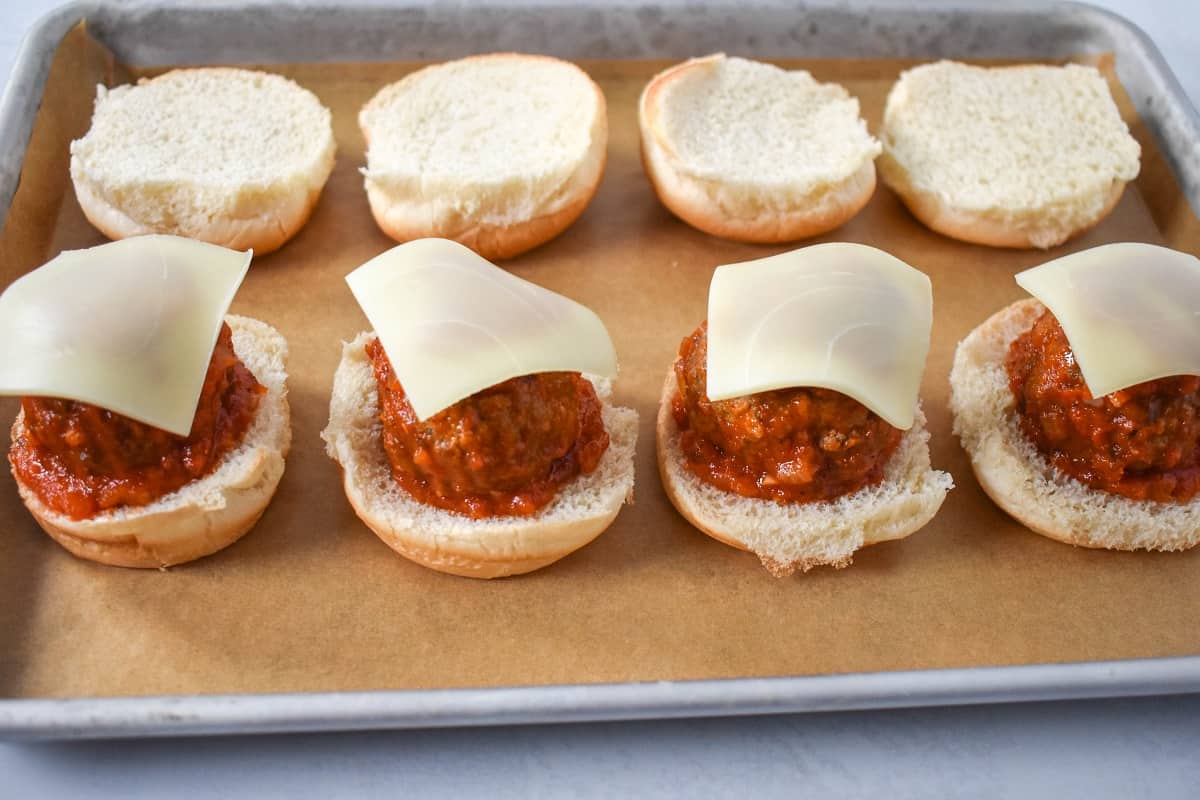 Four meatball sliders being put together on a baking sheet lined with parchment paper. 