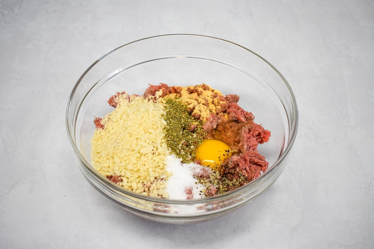 The ingredients for the meatballs before being combined added to a large, glass bowl.