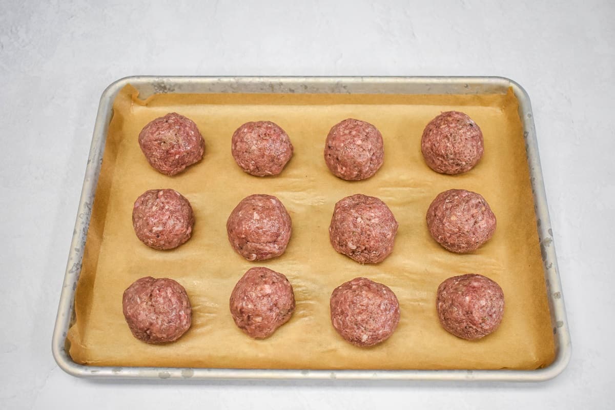 Twelve meatballs neatly arranged on a baking sheet lined with parchment paper.