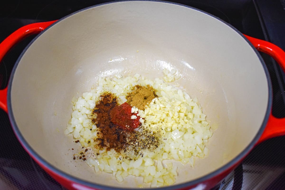 Diced onions, minced garlic, tomato paste, and spices in a large white and red pot.