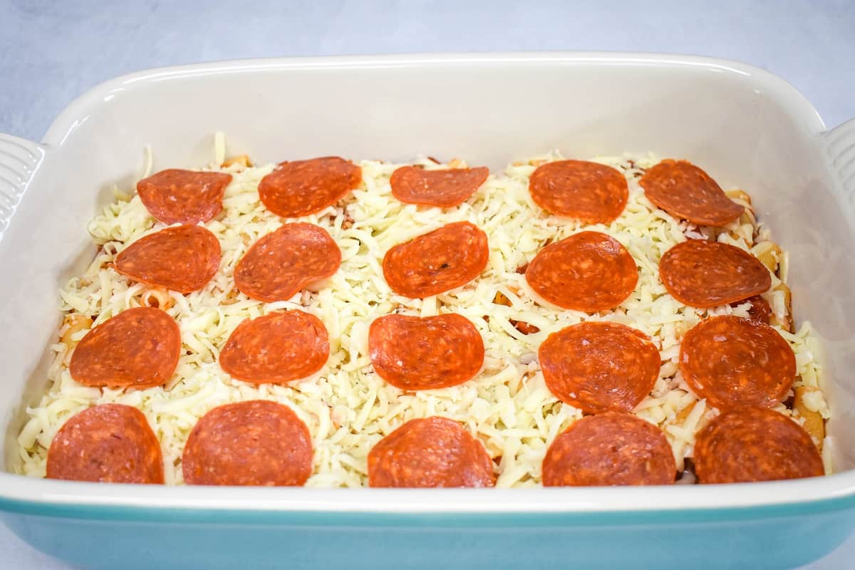 Shredded mozzarella cheese and pepperoni arranged on the pasta in a large baking dish.