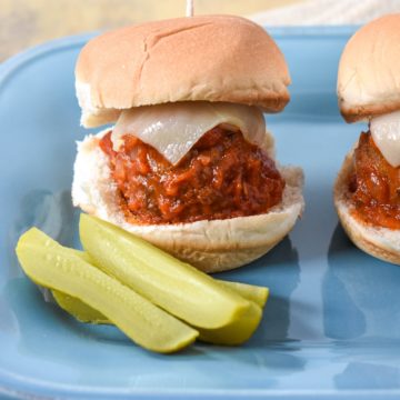 A meatball slider with pickle spears on the side set on a light blue plate.