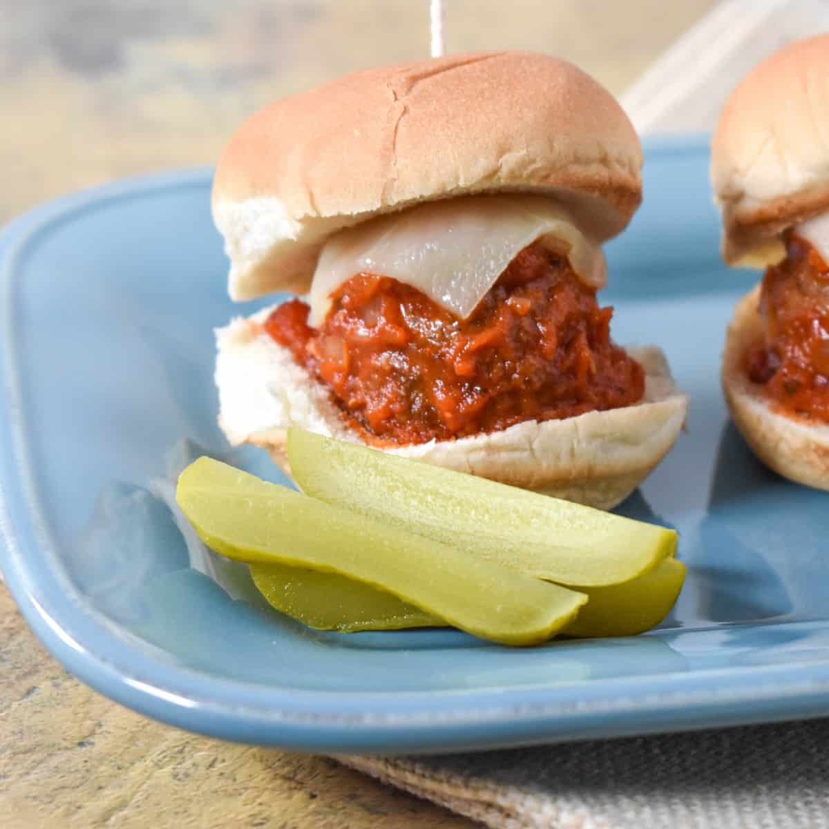 A close up of one finished little sandwich with pickle spears on the side served on a light blue plate.