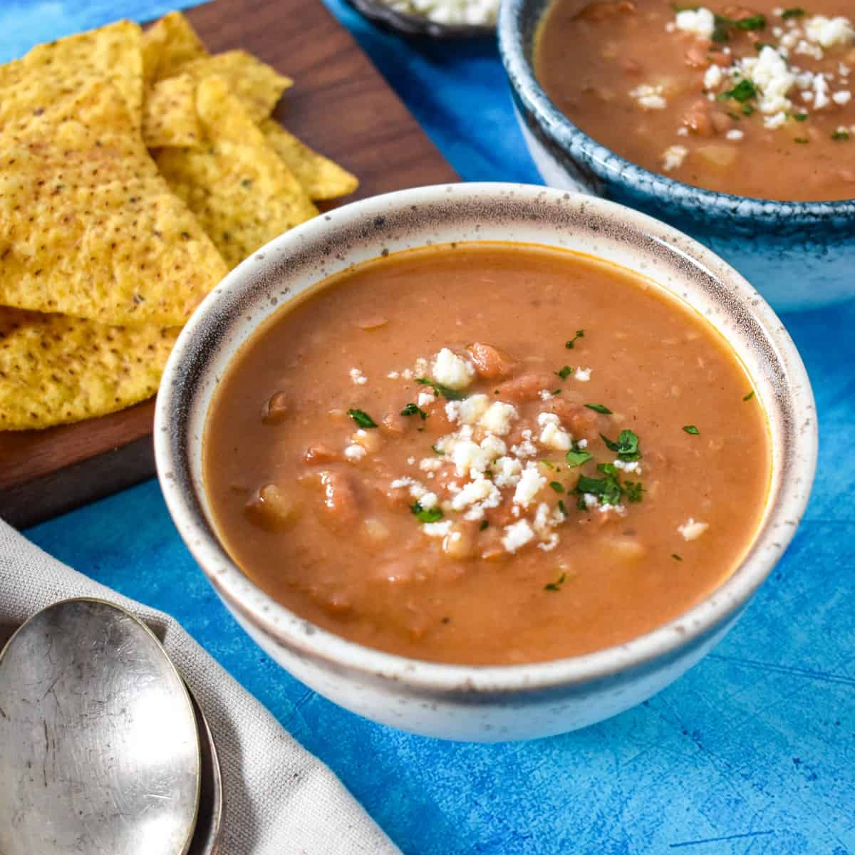 The pinto bean soup garnished with queso fresco and parsley and served in a white bowl with a beige rim.