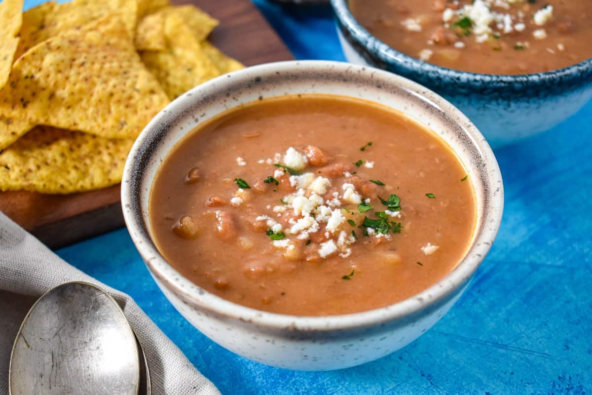 The finished soup in a white and beige bowl, served with tortilla chips and set on a blue table.