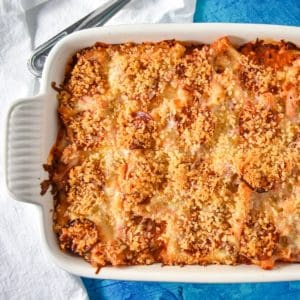 The finished pizza pasta bake in a white casserole dish set on a blue table with a white linen.