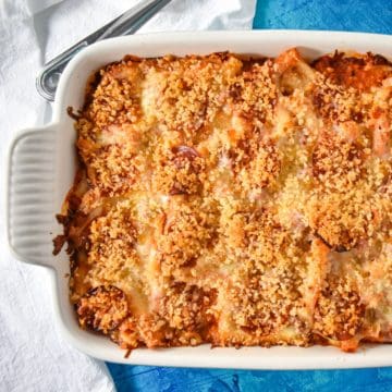 The finished pizza pasta bake in a white casserole dish set on a blue table with a white linen.