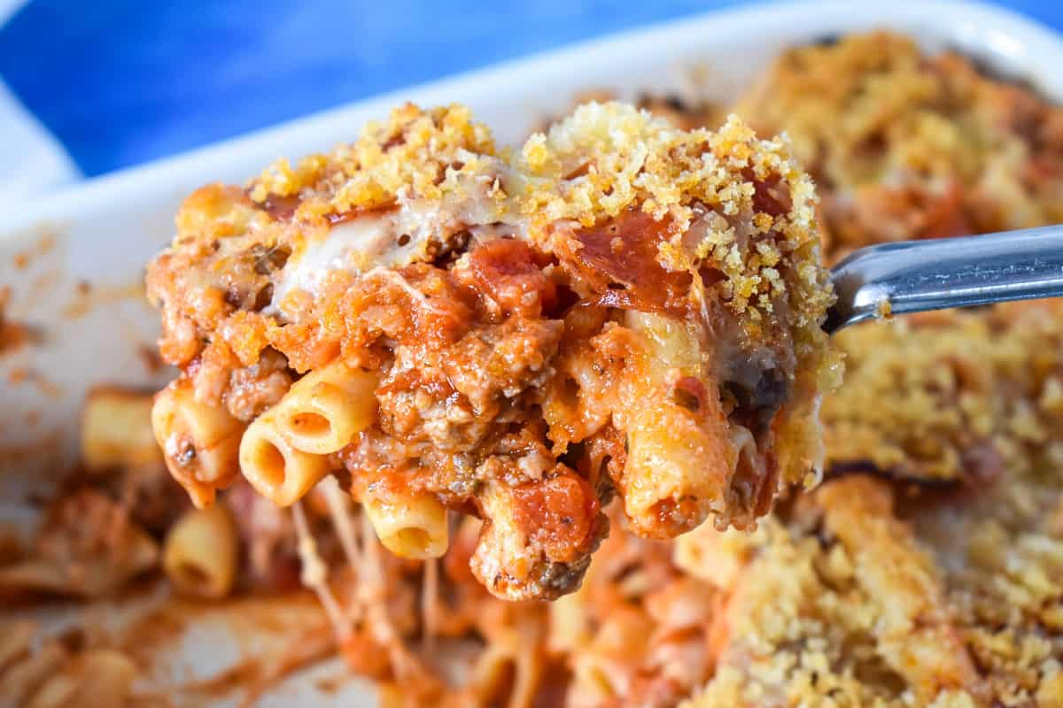 A portion of the pizza pasta bake held up by a serving spoon over the baking dish.