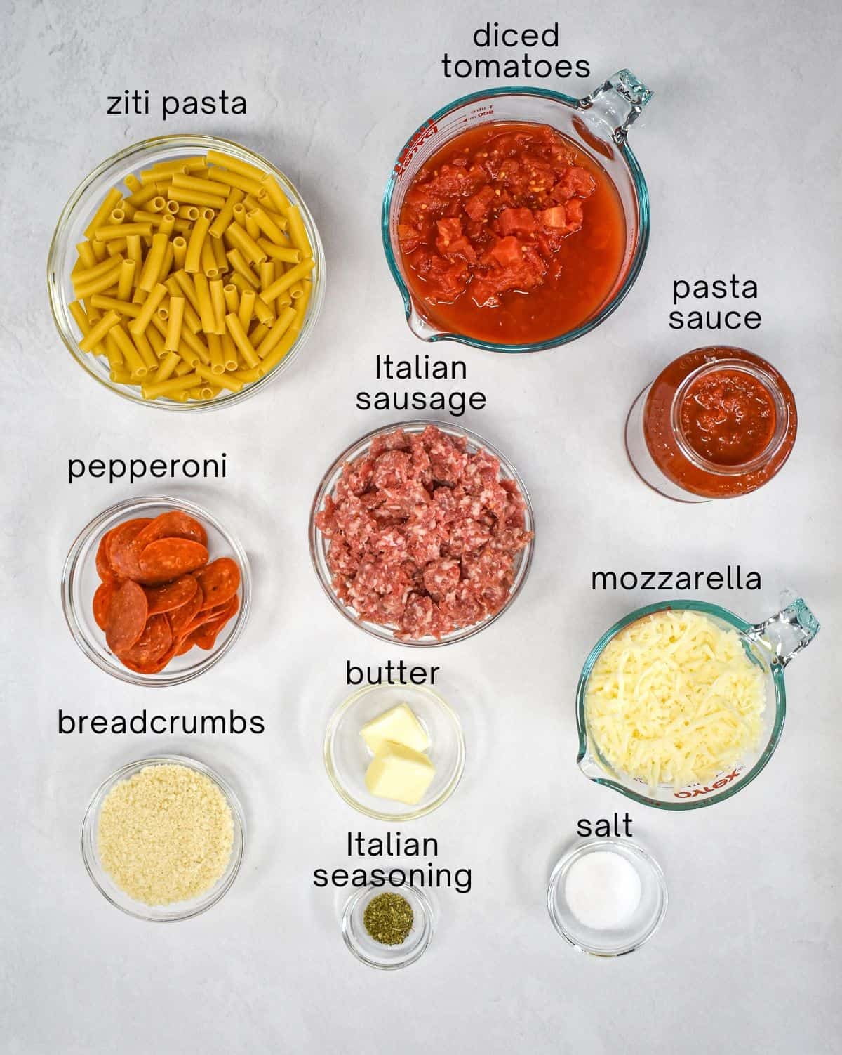 The ingredients for the dish arranged in glass bowls and set on a white table, with each one labeled in small black letters.