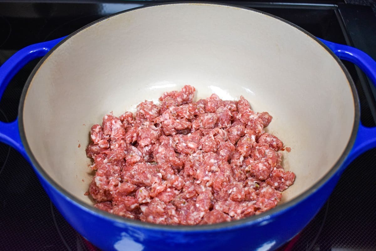 Bulk sausage added to a large white and blue pot.