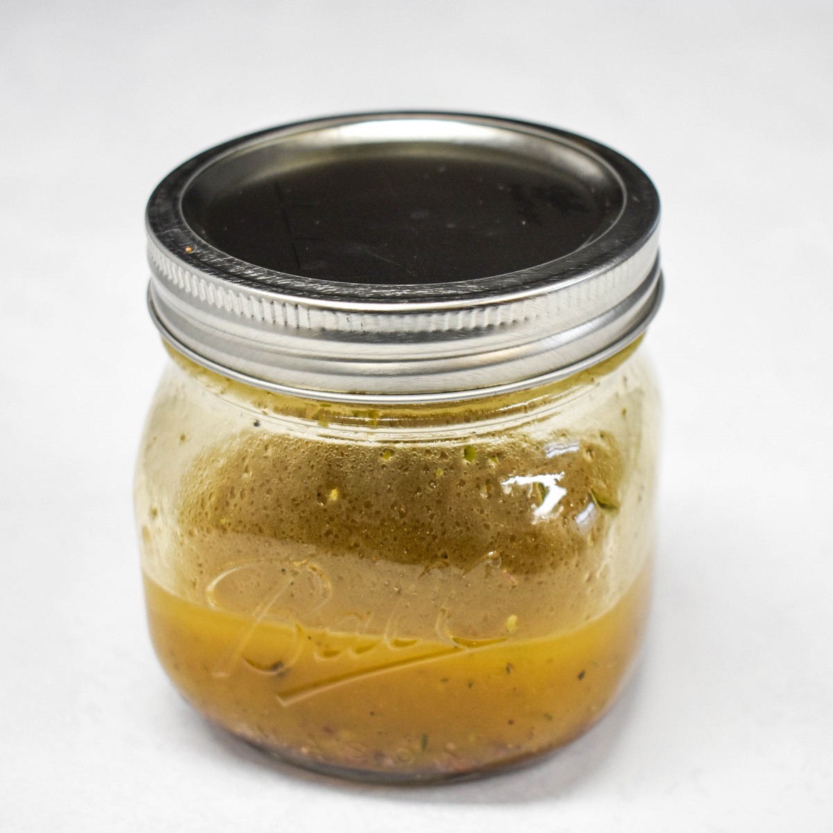 Homemade Italian dressing in a small canning jar, set on a white table.