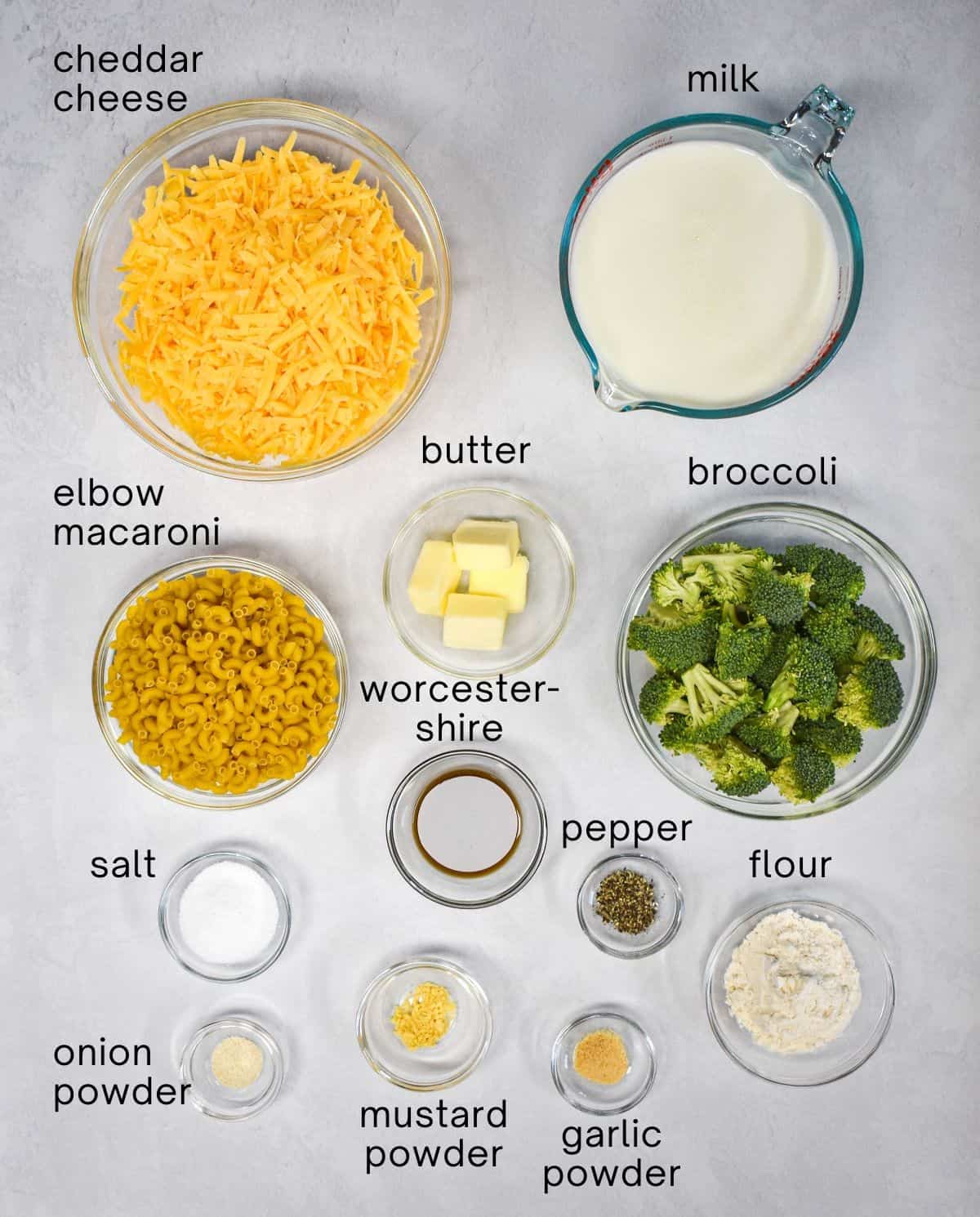 The ingredients for the dish arranged in glass bowls, set on a white table, and labeled in small, black letters.