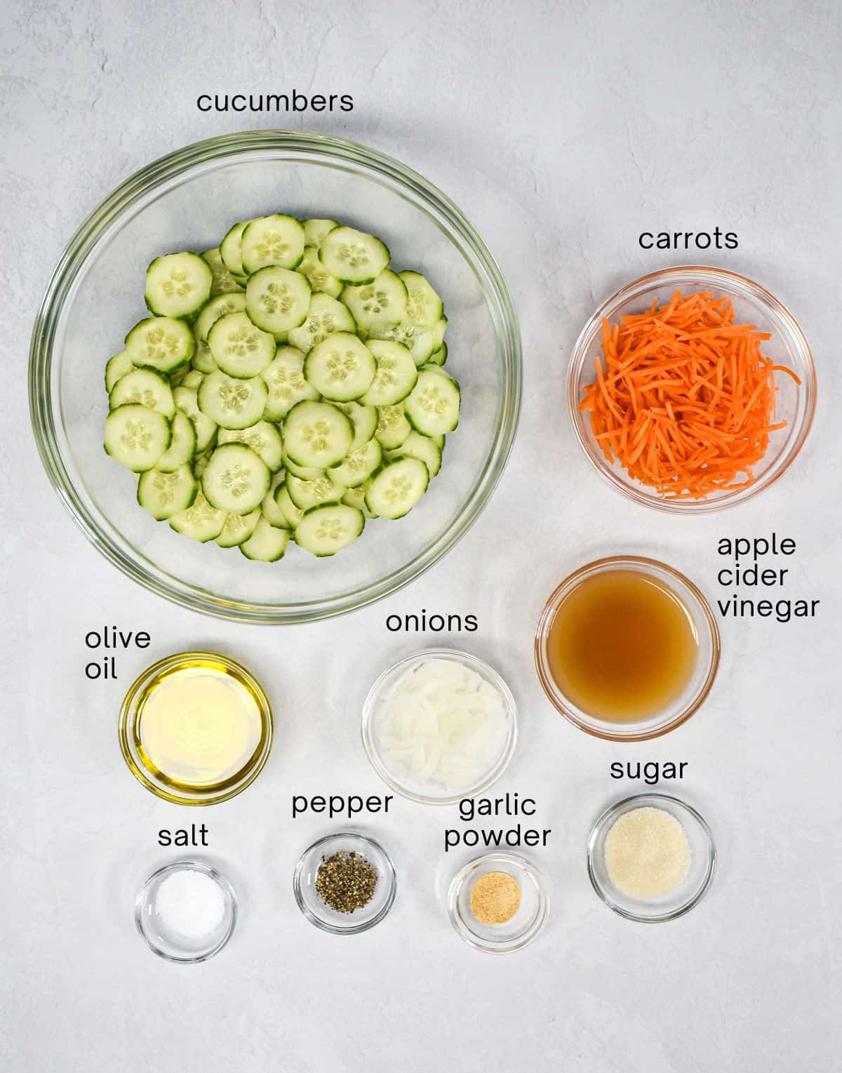 The ingredients for the side dish prepped and arranged in glass bowls on a white table, with each labeled in small, black letters.