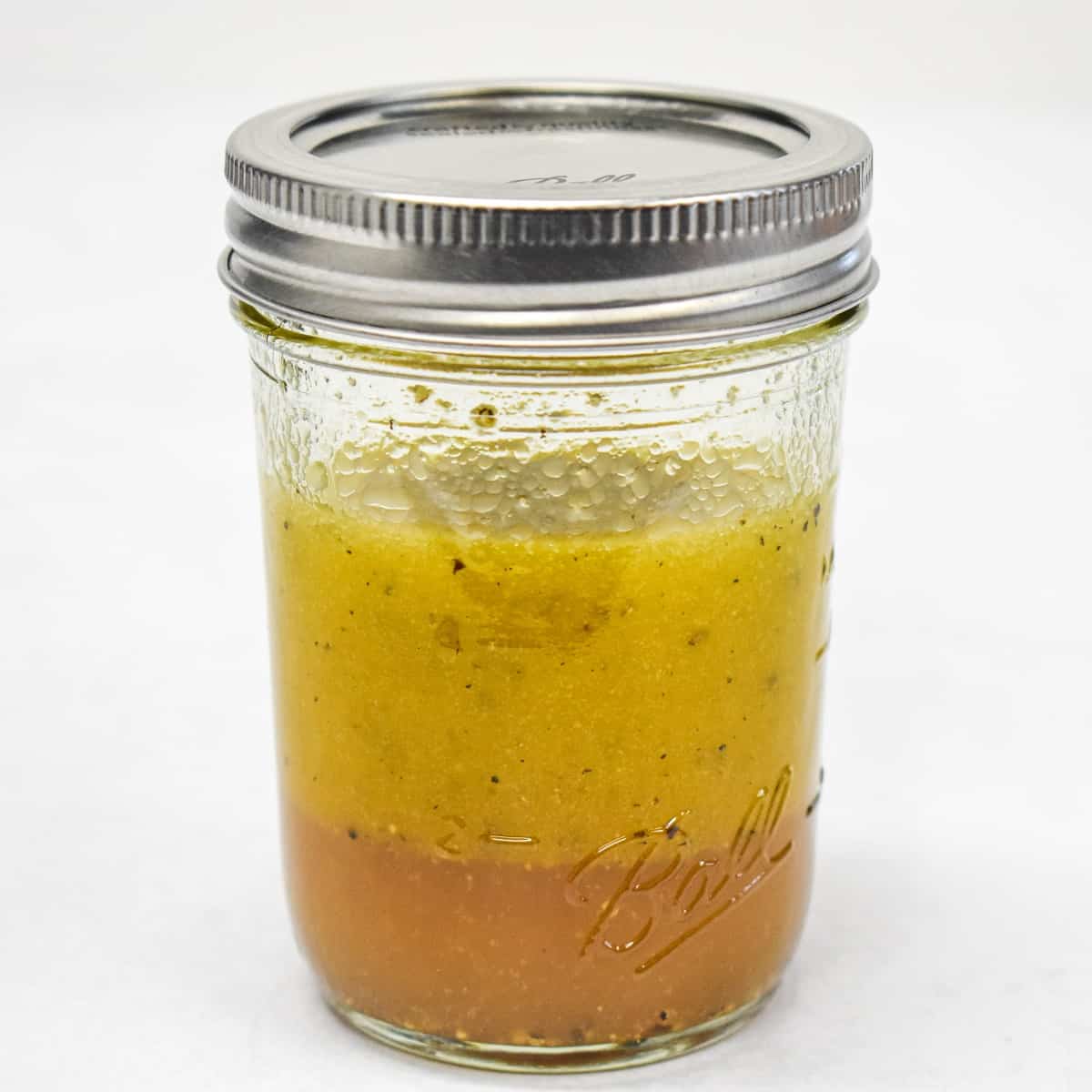 The dressing for the salad in a small canning jar set on a white table.