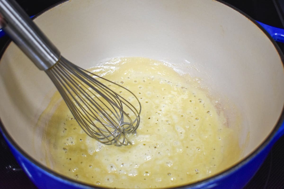 Butter and flour combined with a whisk in a large, white and blue pot.