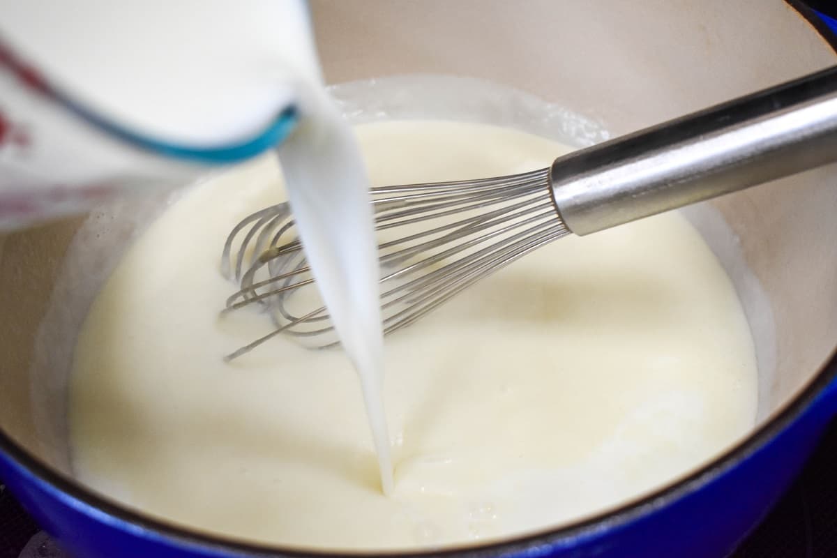 Milk being added to a large white and blue pot with a whisk to the right side.