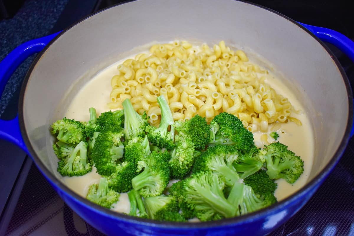 Steamed broccoli and cooked macaroni added to the cheesy cream sauce in the pot.