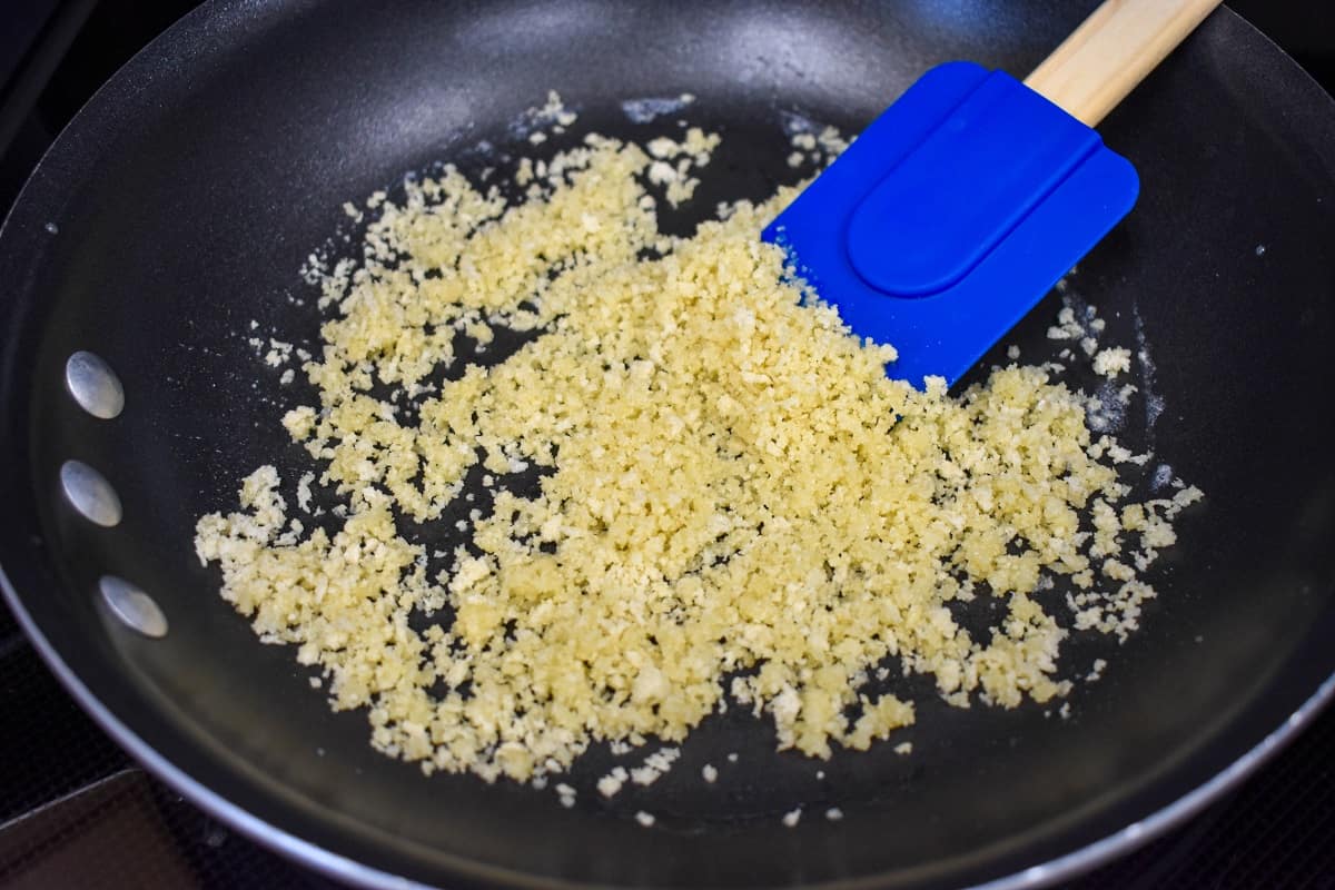 Panko breadcrumbs combined with melted butter cooking in a non-stick skillet and mixed with a blue silicone spatula.