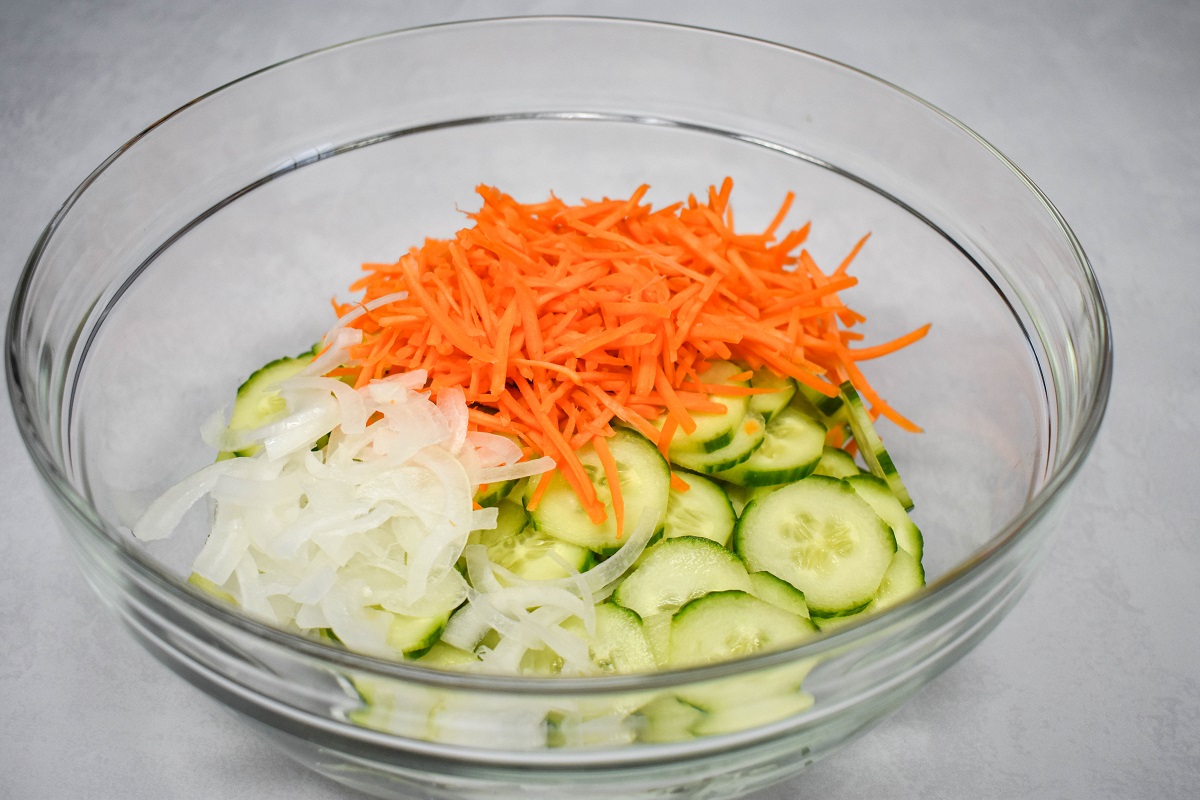 Sliced cucumbers, matchstick carrots, and sliced onions in a large, glass bowl.