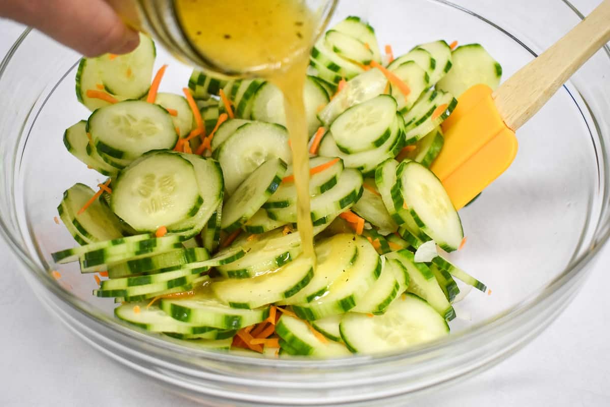 Dressing being added to the ingredients in a glass bowl.