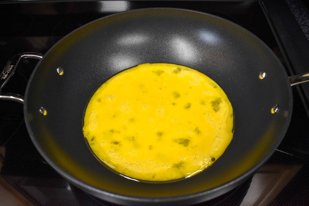 Uncooked whisked eggs added to a large, black skillet.