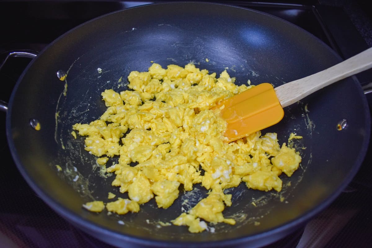 Scrambled eggs in a large, black skillet with an orange silicone spatula to the right side.