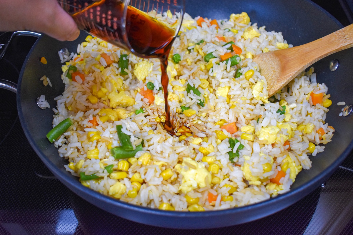 Soy sauce being added to the rice mixture in the skillet.