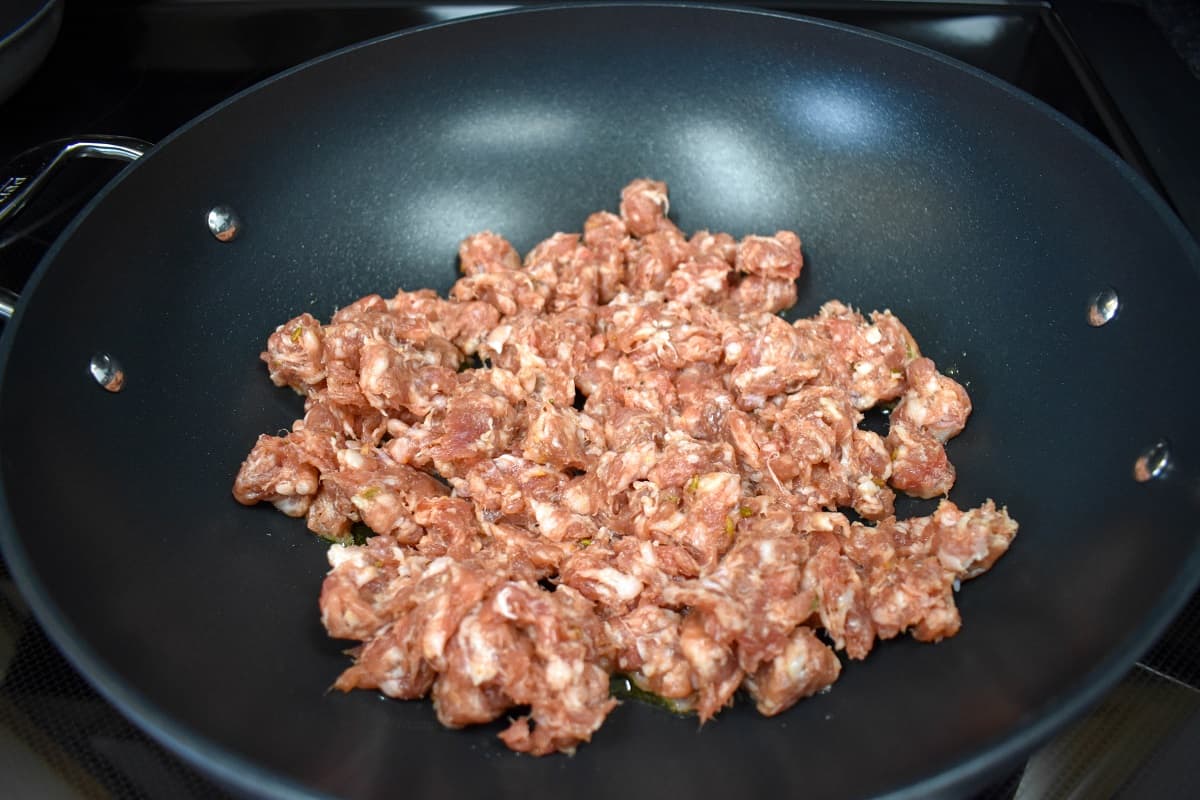 Torn pieces of Italian sausage added to a large, black skillet.