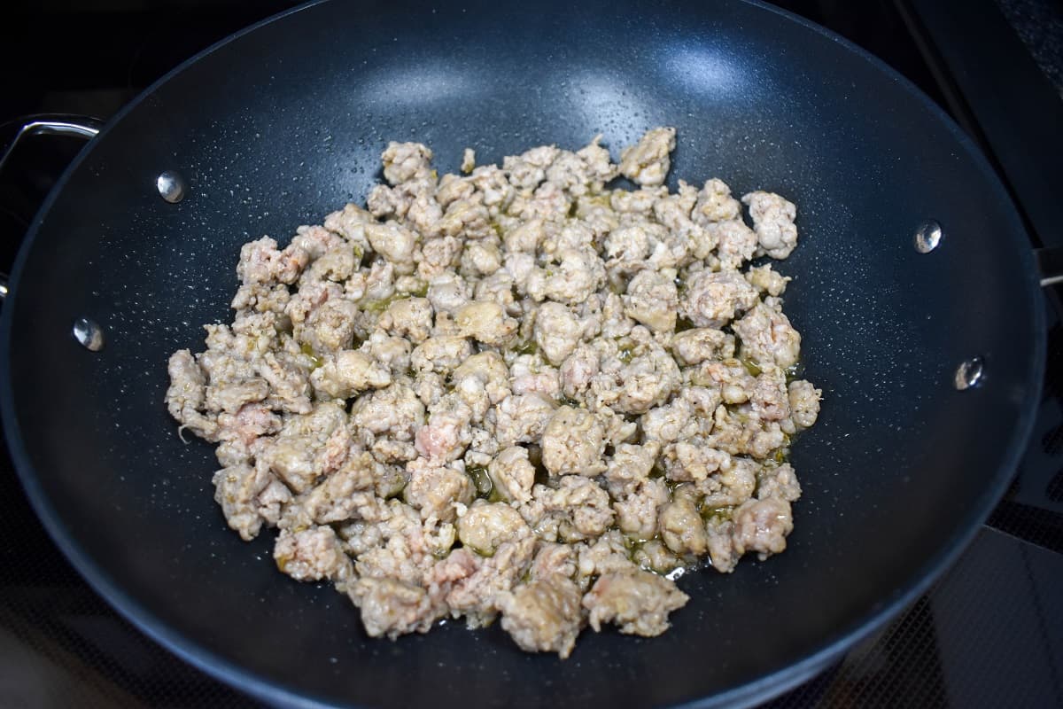 Browned Italian sausage pieces in a large, black skillet.