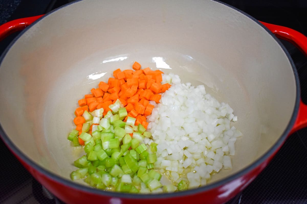Diced onions, carrots, and celery added to a large, red and white pot.
