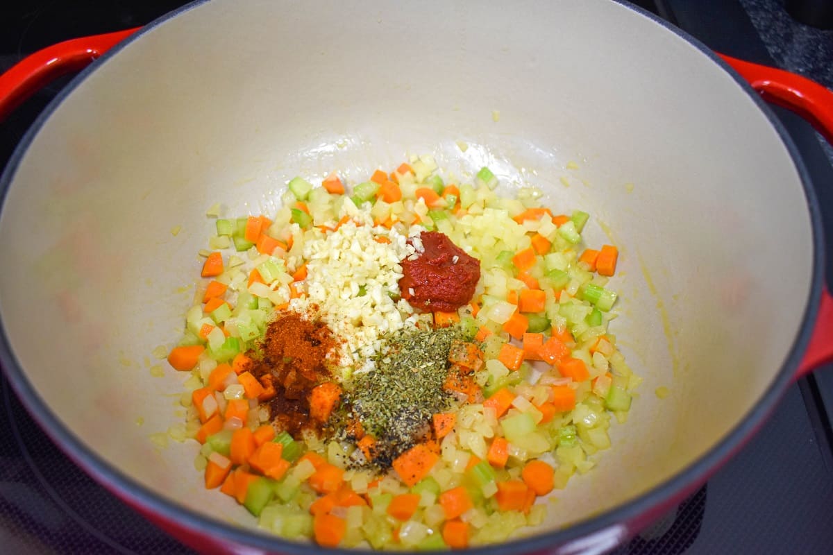 Minced garlic, spices, and tomato paste added to sautéed onions, carrots, and celery in a large pot.