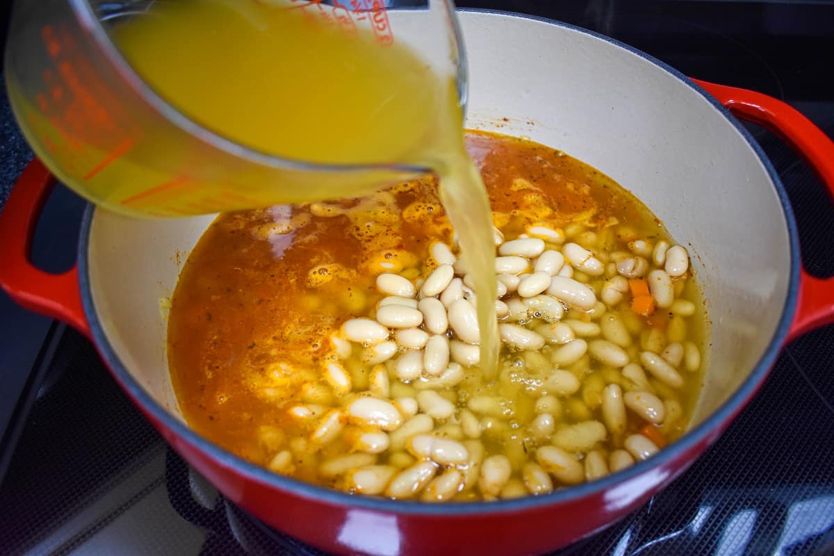 Chicken broth being added to the beans and vegetables in the pot.