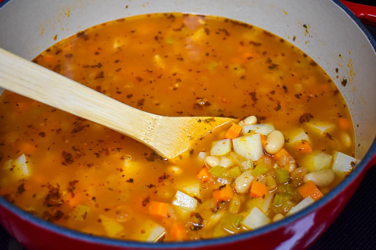 The soup in a pot with a wooden spoon stirring the potatoes added to the remaining ingredients.