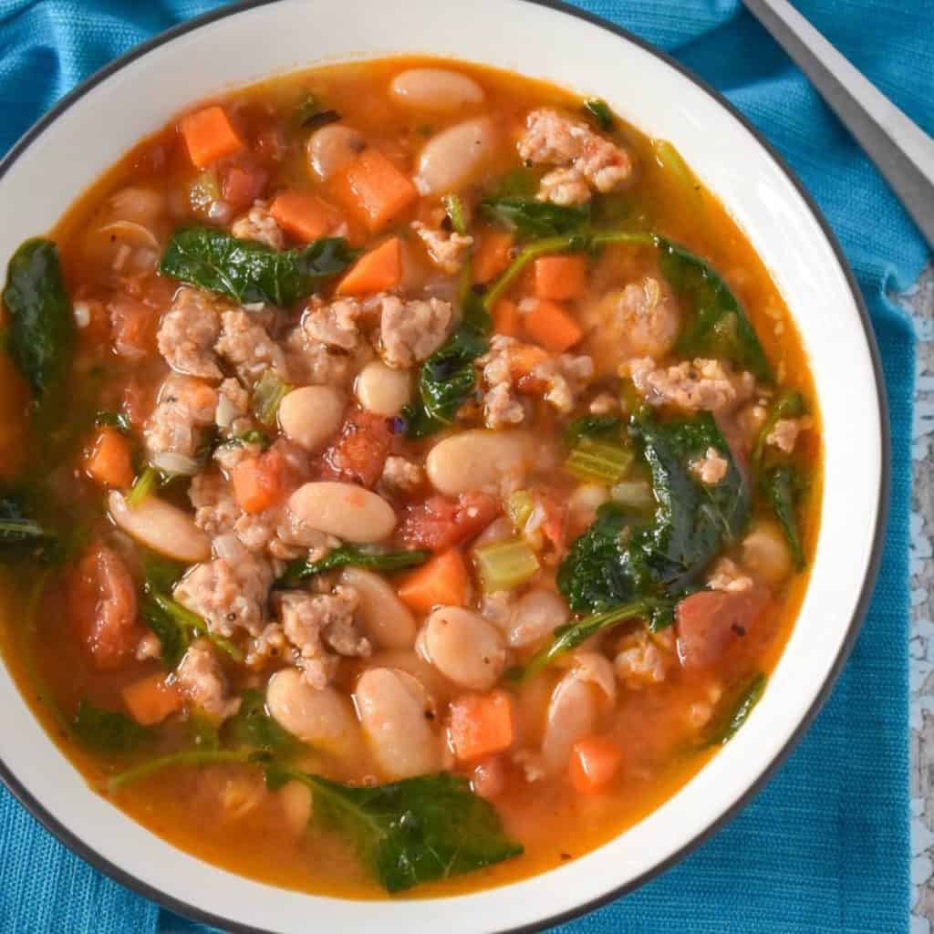 The sausage white bean soup served in a white bowl on a turquoise linen.