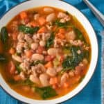 The sausage white bean soup served in a white bowl on a turquoise linen.