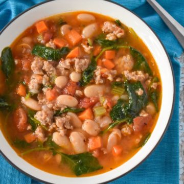 The sausage white bean soup served in a white bowl on a turquoise linen.