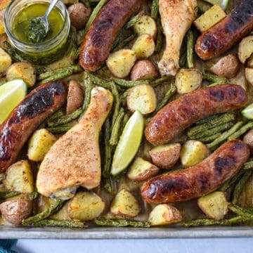 The baked chicken and sausage with potatoes and green beans served with lime wedges and chimichurri sauce.