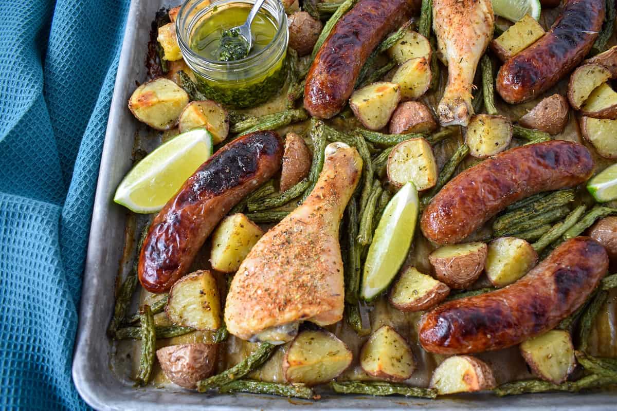 The baked chicken and sausage with potatoes and green beans served with lime wedges and chimichurri sauce.