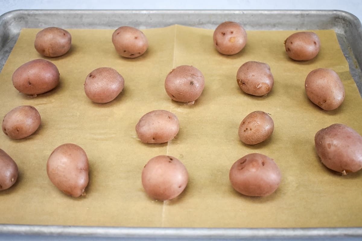 Cooked red potatoes arranged on a large baking sheet lined with parchment paper.