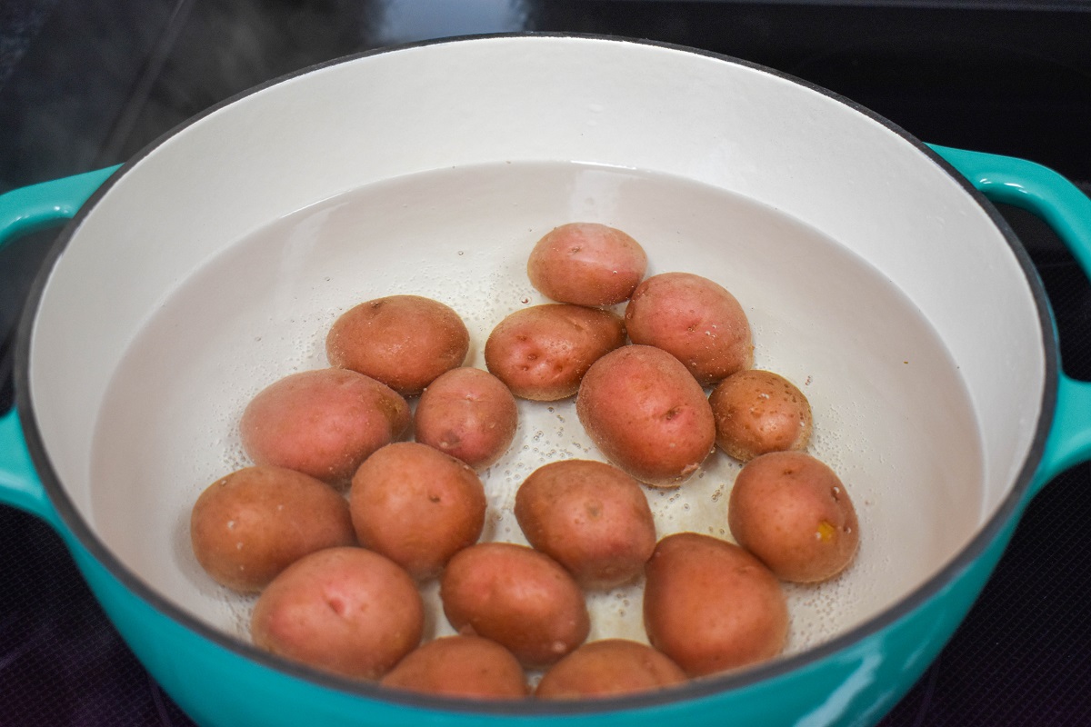 Small red potatoes covered with water in a teal and white pot.