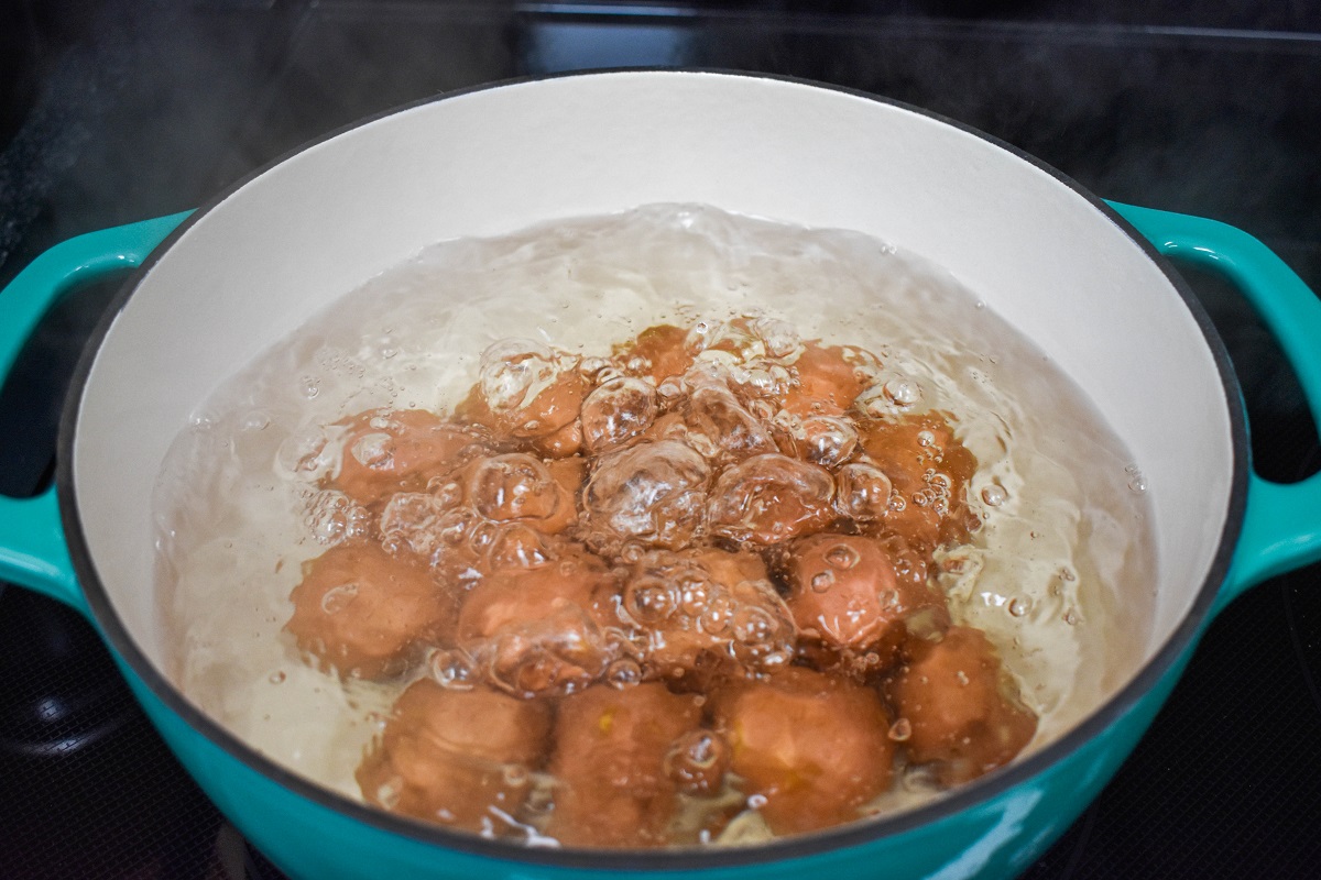 Small red potatoes in boiling water in a teal and white pot.