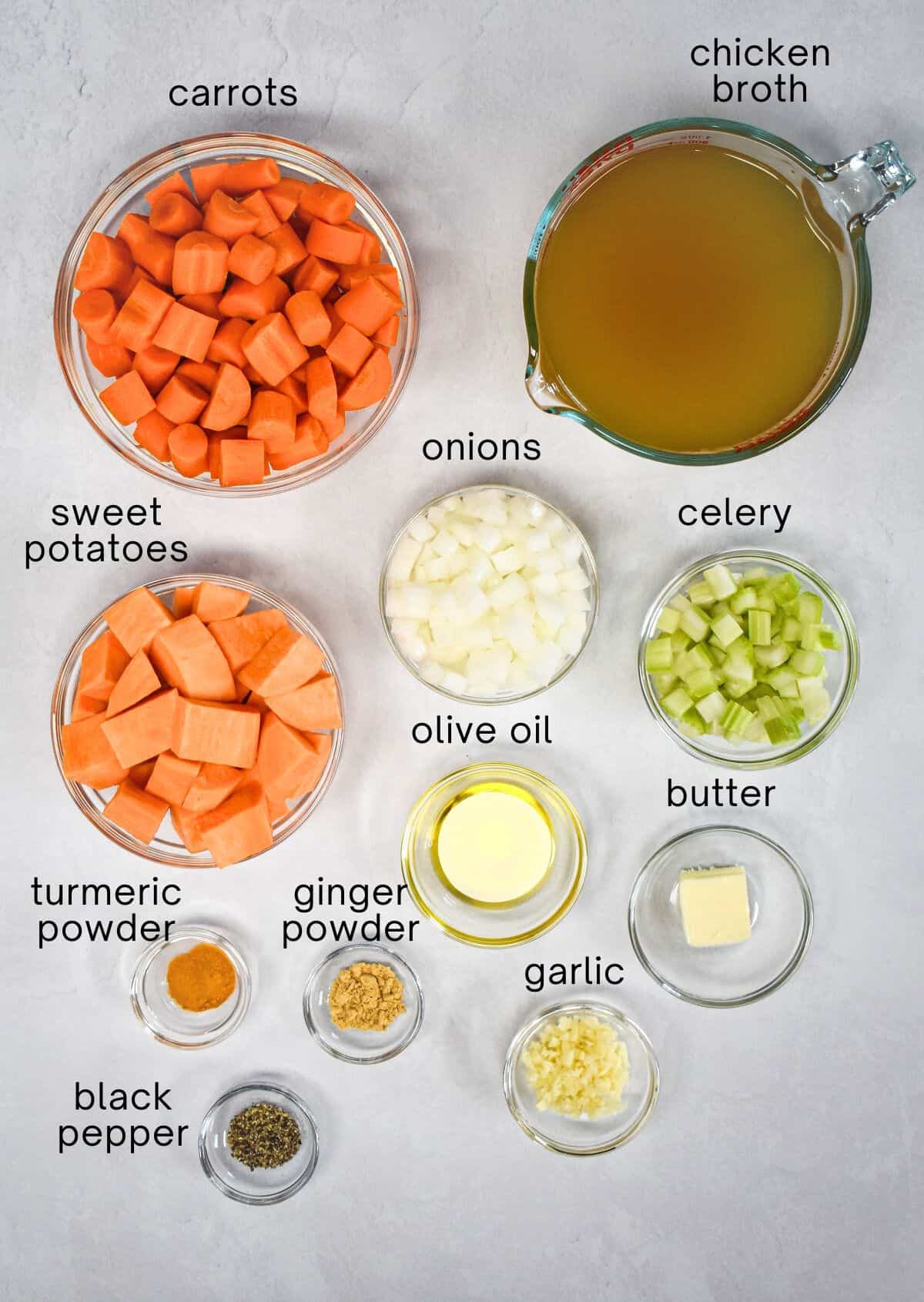 The ingredients for the soup arranged in glass bowls set on a white table with each labled in small, black letters.