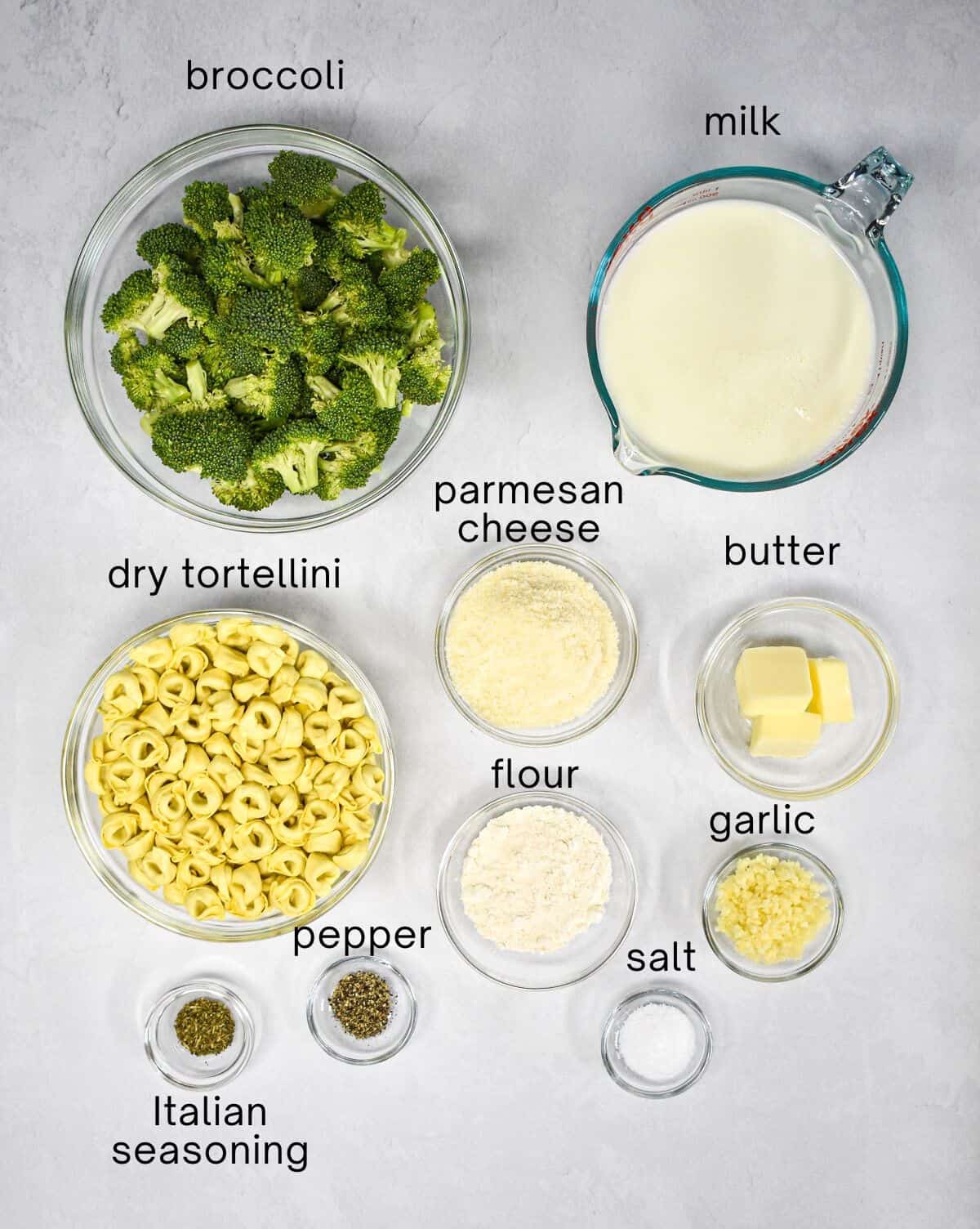 The ingredients for the pasta dish prepped and arranged in glass bowls with each labled with small black letters.