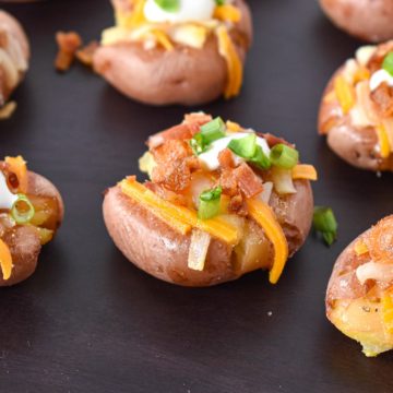 A few loaded smashed potatoes on a black cutting board.