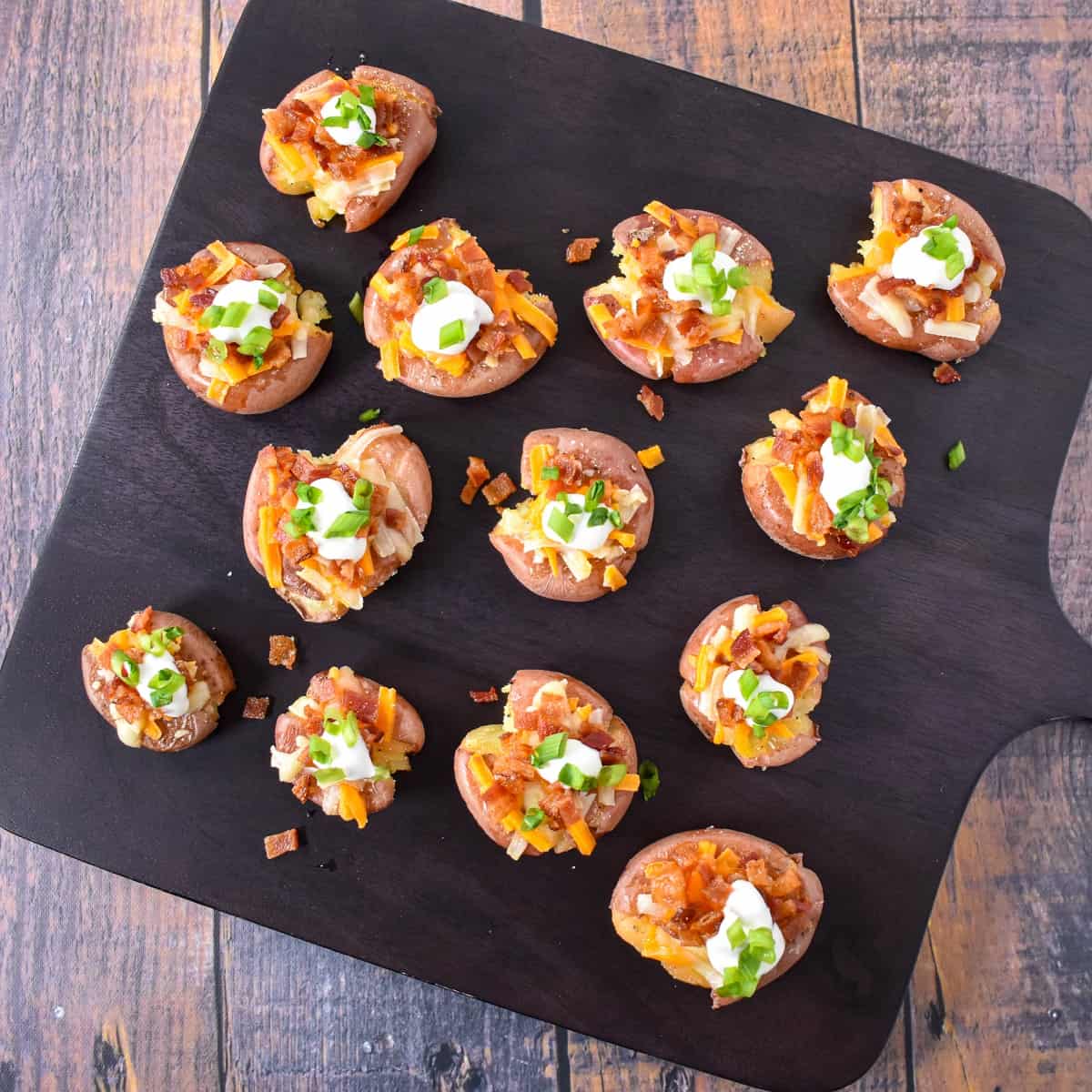 The finished potatoes arranged on a black cutting board set on a wood table.